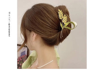 Detail of wheat ear metal hair claw clip in gold and green on model's hairstyle