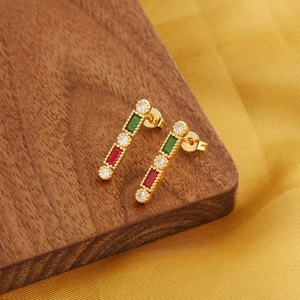 Champagne gold rectangular earrings with red, green and white gemstones on wood surface