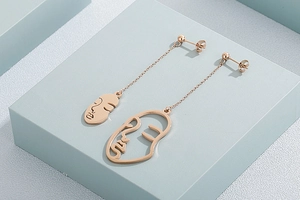 Détails de boucles d'oreilles or rose avec visages abstraits et longues chaînes pendants