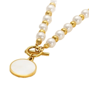 Collana di perle con chiusura OT dorata e ciondolo in conchiglia su sfondo bianco