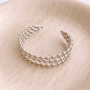 Detail of a three-row silver bead open cuff bracelet on a beige ceramic plate