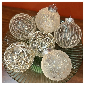 Close-up of champagne mesh Christmas ornaments in a green glass bowl on wood table