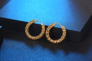 Detail of gold hoop earrings featuring intricate beaded texture on a black display box