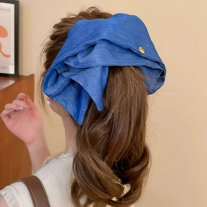 Blue denim bow hair clip with gold emblem shown on a wavy ponytail from a back view
