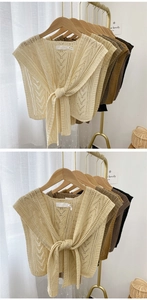 Close-up of beige knit shawl with hollow patterns and front lace-up detail on hangers