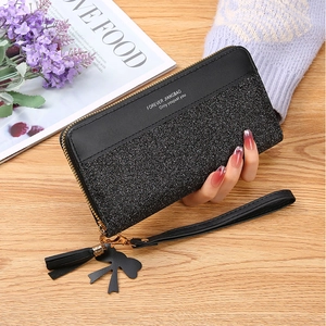 Detail of black long wallet with glitter texture, tassel charm and bowknot on wooden table