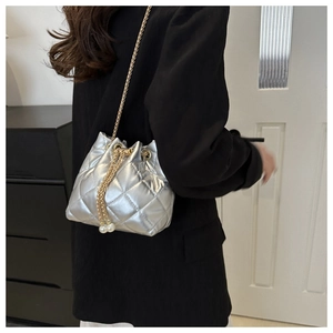 Silver quilted bucket bag featuring a metallic finish, gold chain, and pearl drawstrings