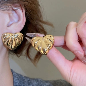 Macro detail of large gold heart earrings with elegant textured scallop pattern on model