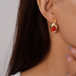 Macro view of gold teardrop earring with vibrant red rhinestone inlay on model