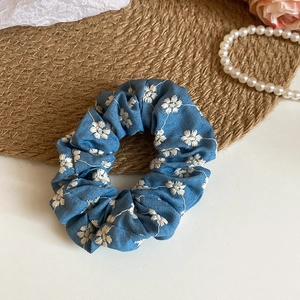 Detail of blue pleated fabric scrunchie with white daisy embroidery on straw mat