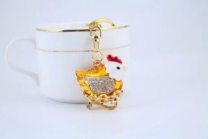 Detail of a sparkling rhinestone chicken keychain resting against a gold-rimmed white teacup