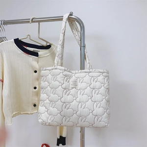 Close-up of white quilted tote bag featuring rabbit embroidery and a woven label detail
