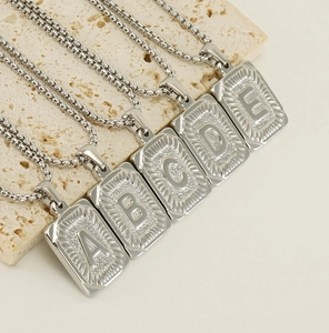 Macro shot of silver square letter pendants A to E on stone, minimalist steel necklace