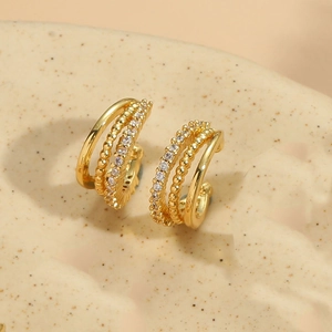 Detail of three-layer gold huggie earrings with cubic zirconia on a ceramic background