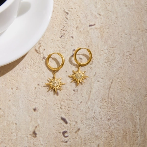 Gold titanium sun earrings with rhinestones on a minimalist stone background