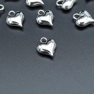 Three-dimensional silver heart charms for DIY jewelry making on a dark textured background