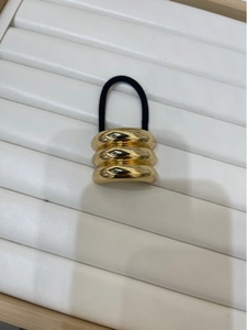 Detailed view of the gold triple-layer ring buckle with black elastic hair tie on display