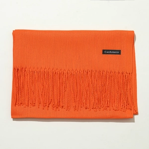 Detail view of smooth orange cashmere scarf with soft fringes on a white background