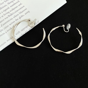 Macro shot of silver twisted hoop earrings with irregular flowing design on black fabric