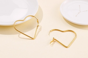 Close-up of golden heart earrings with twisted rope texture on white ceramic plates
