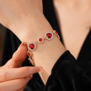 Dettaglio ravvicinato di un bracciale vintage dorato con pietre a cuore rosse e piccoli diamanti