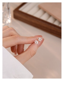 Macro detail of elegant S999 sterling silver hollow rose flower stud earrings on fingers