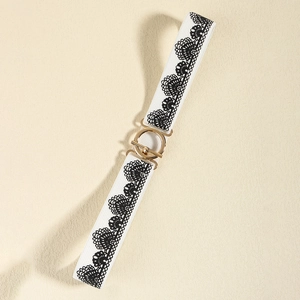 White elastic waist belt with black lace trim and golden buckle on beige textured background