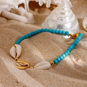 Bohemian anklet with blue beads and natural shells lying on a sandy beach setting