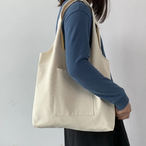 Detail of beige canvas tote bag with large front pocket carried by a model over the shoulder