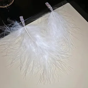 Elegant white feather tassel earrings with sparkling zircon studs on a textured background