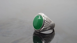 Macro detail of men's titanium ring featuring an oval green gemstone with engraved texture