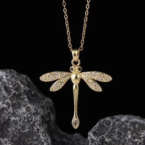 Macro shot of gold dragonfly pendant with white and black crystals on dark stone