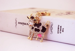 Close-up of a sparkling crystal-encrusted cow keychain on a book with golden details