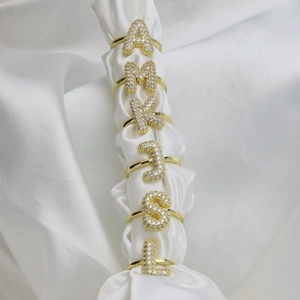 Macro detail of gold bubble letter rings with cubic zirconia on white satin display