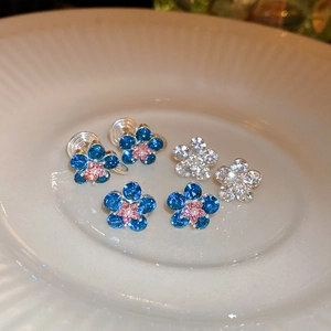 Sparkling crystal flower stud earrings with blue and clear petals on a ceramic tray
