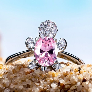 Silver turtle ring with pink oval gemstone and micro-pave crystals on light blue sand