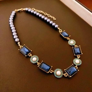 Detail of double-layer necklace with dark grey pearls and blue gemstones in gold setting