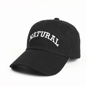Detail of white 'NATURAL' letter embroidery on a black cotton baseball cap surface