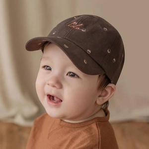 Close-up of a dark brown baby baseball cap with white hola embroidery on a toddler