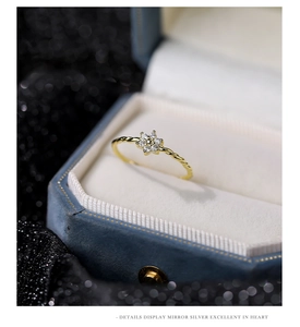 Detailed close-up of a twisted gold ring with a zircon flower on a blue velvet box