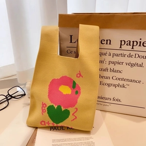 Detailed knit texture of yellow floral tote bag with pink flowers and art book props