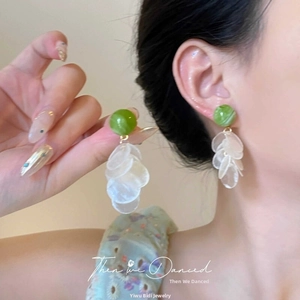 Close-up of sparkling crystal tassel earrings with green cat-eye stone on earlobe