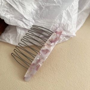 Detail view of acetate comb with pink marble pattern and dark grey metal teeth