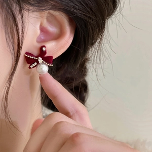 Close-up of a red velvet bow earring with sparkling rhinestones and a white pearl drop