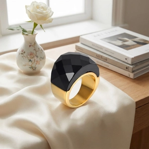 Detail of chunky gold ring with large faceted black crystal on silk fabric background