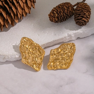 Macro shot of gold hammered metal earrings on a stone slab with pinecone accents