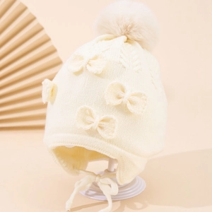 Detailed knit texture of cream winter hat with bow accents and soft faux fur pom-pom