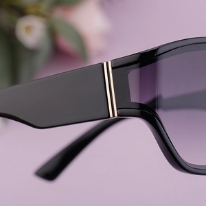 Macro shot of gold hinge detail on square black sunglasses with purple gradient lenses
