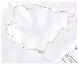Detail of adjustable silver box chain with spring clasp on white silk fabric background