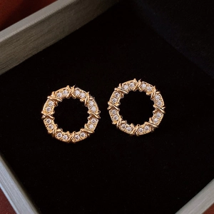 Vue détaillée des boucles d'oreilles rondes dorées avec pierres et design croisé en X